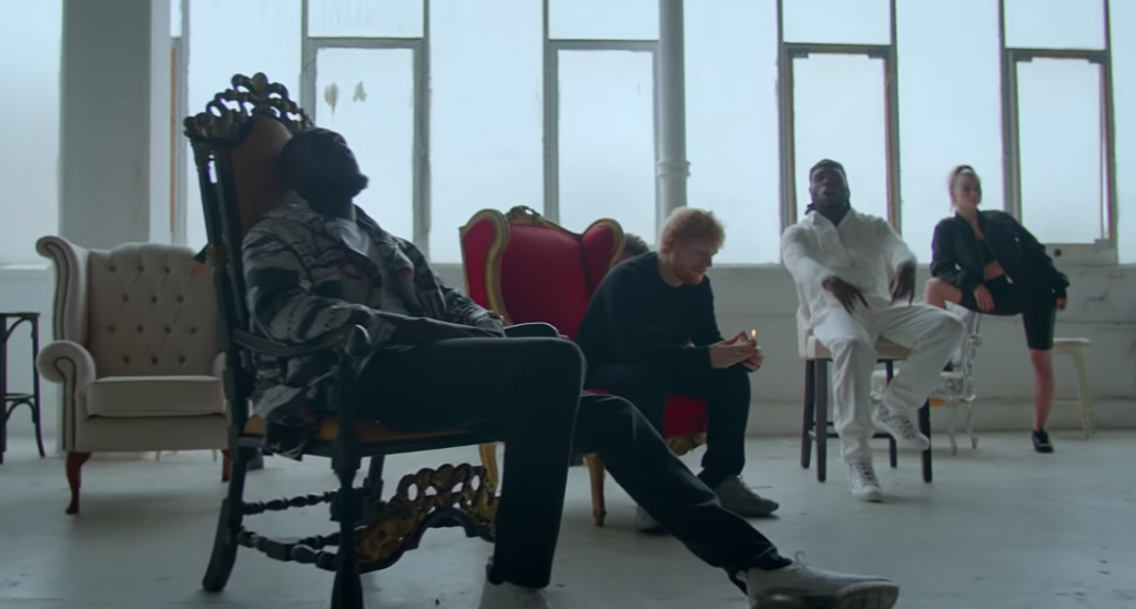 Stormzy, Ed Sheeran, and Burna Boy sitting on elegant chairs in a spacious, light-filled room, taken from the 'Own It' music video. The setting features a mix of vintage and modern aesthetics, perfectly capturing the collaborative energy of the track.