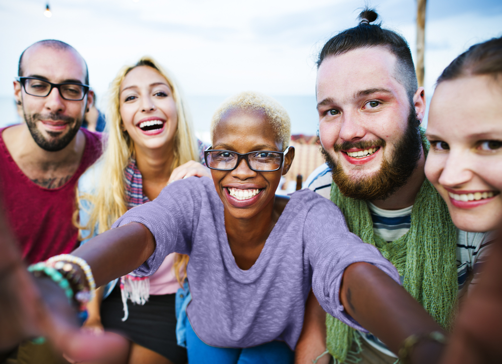 A diverse group of friends smiling and taking a selfie outdoors, representing the joy of moving abroad and fitting in. Featured on Raided by Tintin.