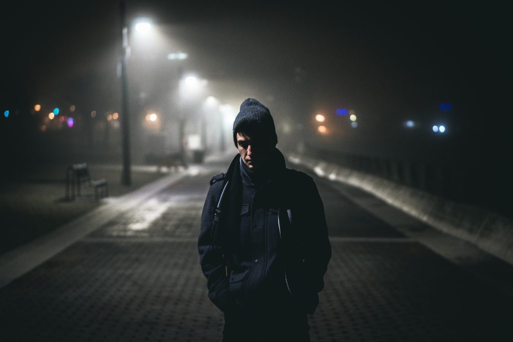 A solitary figure walking on a dimly lit street at night, symbolizing the emotional journey of moving abroad and fitting in. Featured on Raided by Tintin.