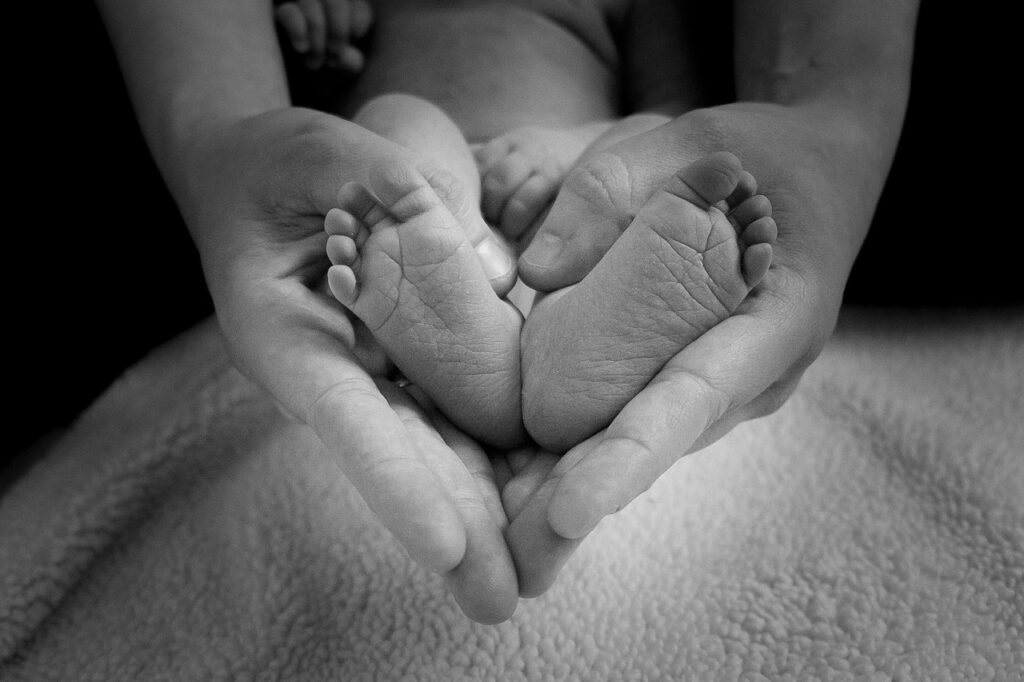 A black-and-white photo of a parent’s hands gently holding a newborn's feet, symbolizing love and care. Image by one_life from Pixabay.