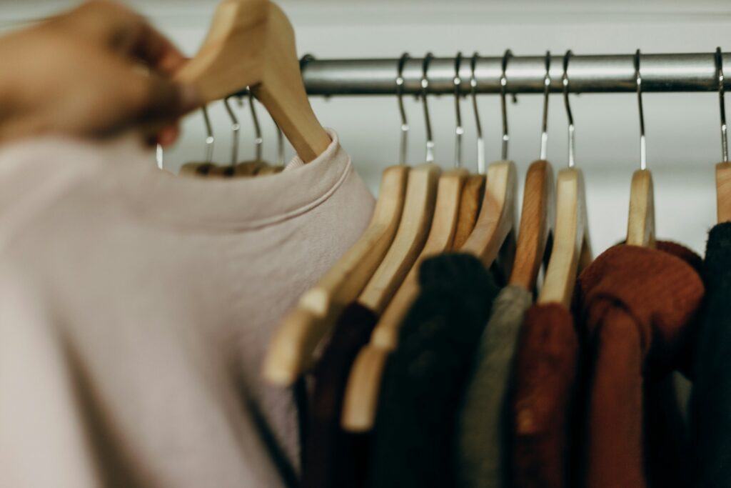 Close-up of a clothing rack with wooden hangers holding a variety of neutral and earthy-toned garments. essential wardrobe checklist Photo by Priscilla Du Preez 🇨🇦 on Unsplash.