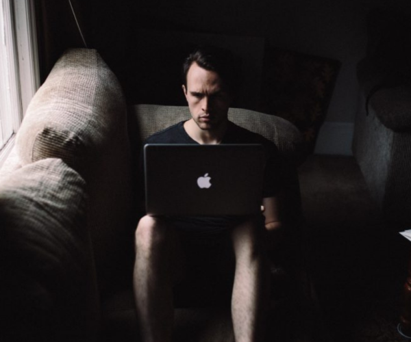 A focused individual sitting in a dimly lit room, intensely working on a laptop, symbolizing the calculated actions of a revenge seeker, also known as the online avenger. Featured in the article 'Types of Cyberbullies: Tackling Digital Harassment with Confidence' on Raided by Tintin.